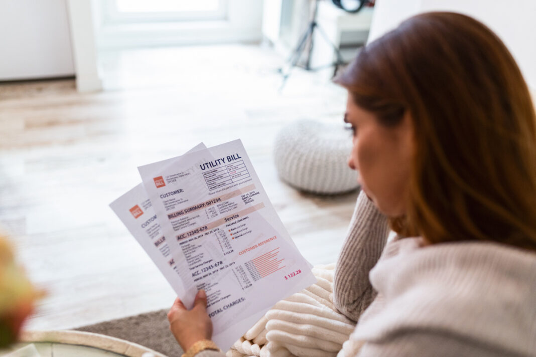 Indoor shot of casually dressed young woman holding papers in her hands, calculating family budget, trying to save some money , having stressed and concentrated look